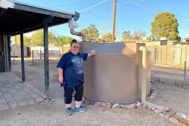 Participant in Tucson's Limited-Income Rainwater Harvesting Loan and Grant Program standing in front of a cistern in her yard